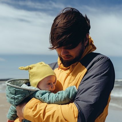 Vater mit Baby warm angezogen am Strand.